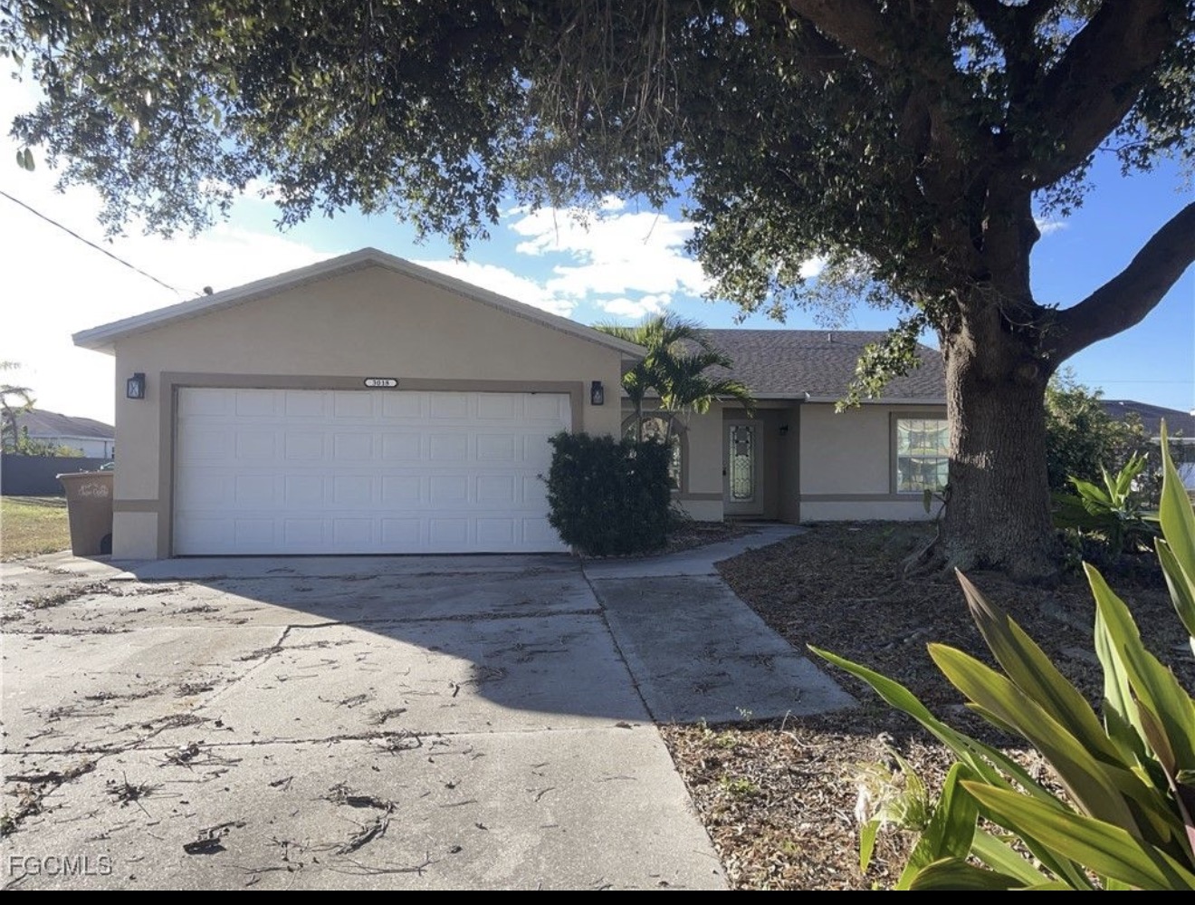 Cape Coral stucco ranch with two-car garage and mature oak tree — example of a storm-damaged home bought as-is